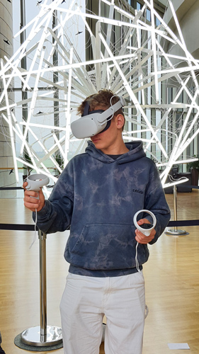 Das Foto zeigt einen Jungen, der eine VR-Brille trägt. Er steht vor einer futuristisch aussehenden Lampe.