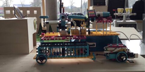 Eine mehrfarbige Robotermaschine, die auf einem Holztisch ausgestellt ist, im Hintergrund sind Modellhäuser zu sehen.